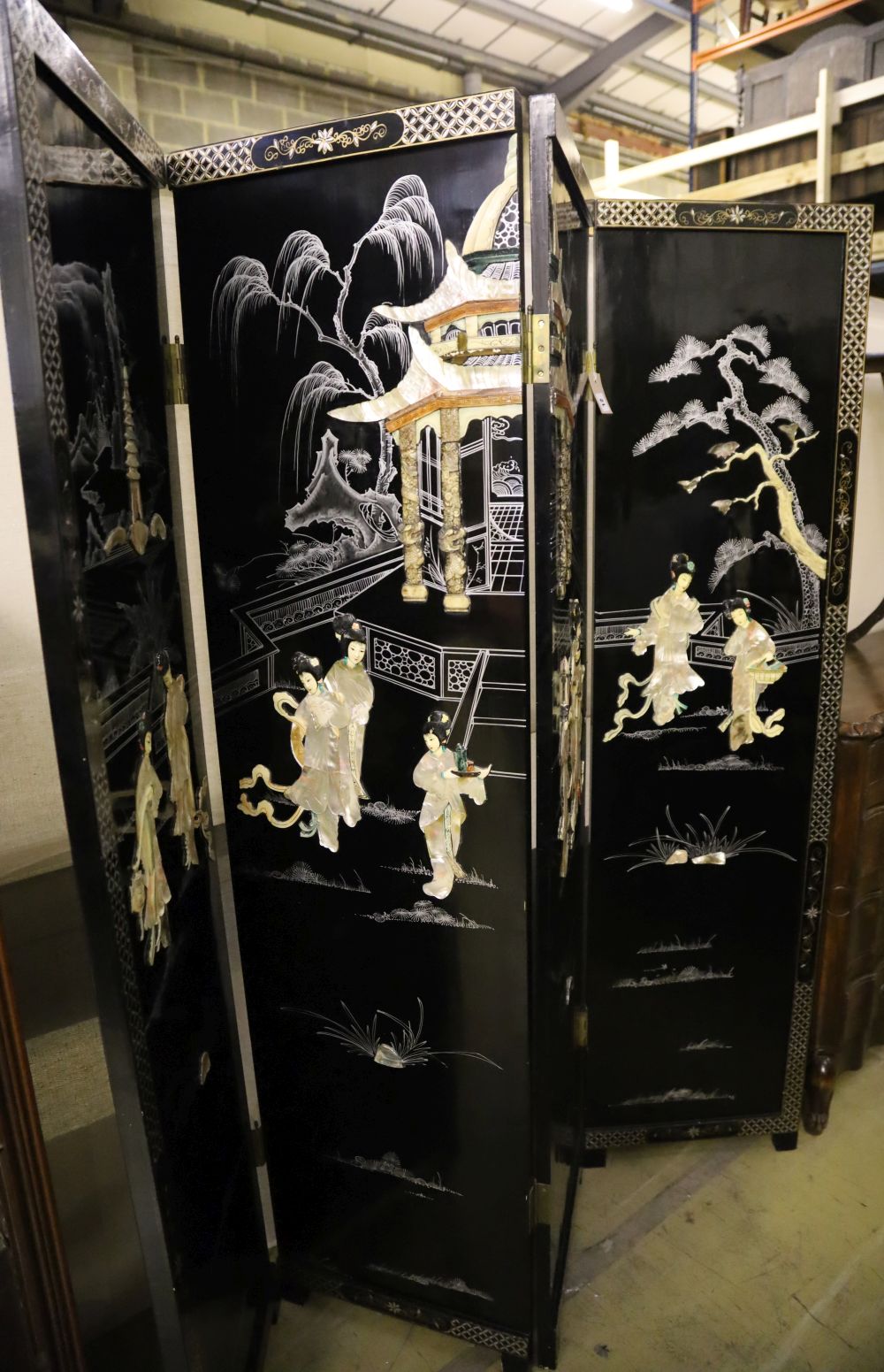 A Japanese black-lacquered and painted four-fold screen with applied decoration of geishas and temple, each panel 46 x 182cm